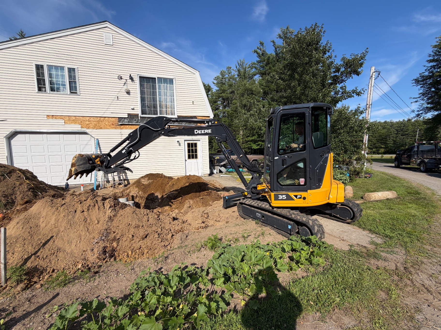 Nate's Septic John Deere 35 mini excavator digging beside a house and garage on a residential septic job