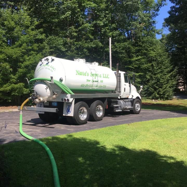 Nate's Septic LLC pump truck on a paved driveway with a green suction hose running across the lawn during a tank pump-out